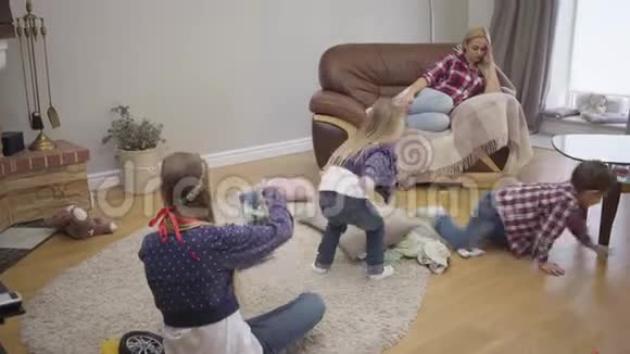 疲惫的高加索女人在沙发上休息她的孩子在玩年轻的儿子和女儿像大女儿一样到处跑视频的预览图
