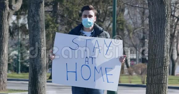 戴着防护面具的年轻人拿着海报呆在家里视频的预览图