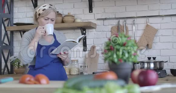成熟的金发女人早晨喝咖啡和阅读食谱的肖像严重的中年退休人员视频的预览图