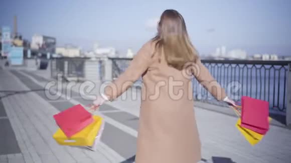 阳光明媚的秋日年轻胖乎乎的女人在河岸上拿着购物袋旋转着高加索妇女视频的预览图