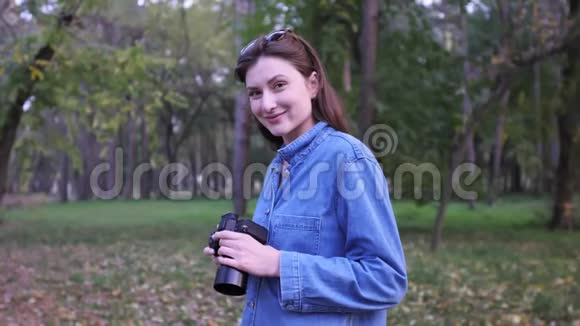一个专业的自由职业者的肖像在秋天的森林日落时手里拿着相机女孩微笑着看着视频的预览图