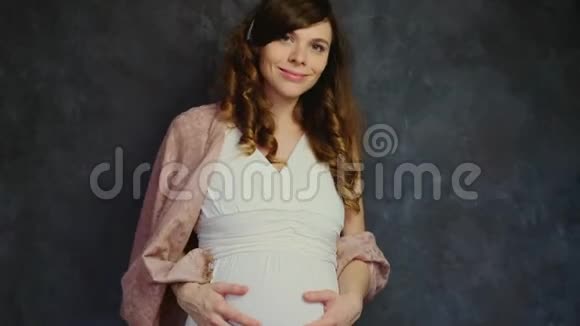 美丽的怀孕年轻女子梦幻般的微笑抚摸着她的腹部期待婴儿概念视频的预览图