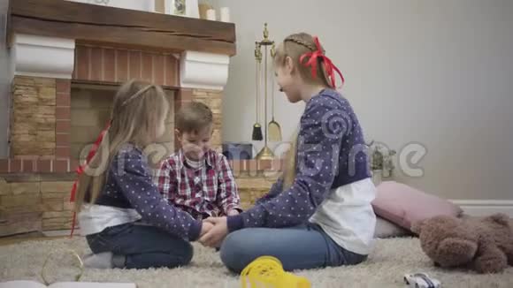 快乐的白种人兄弟和两个姐妹坐在壁炉前互相牵着的手友好的兄弟姐妹视频的预览图