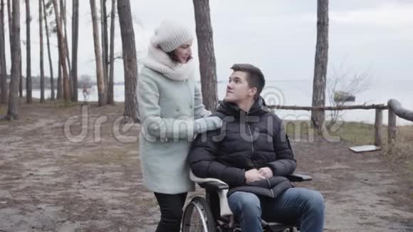 坐在轮椅上微笑的男孩和成年女人说话和牵手的肖像白种人残疾人享受时光视频的预览图