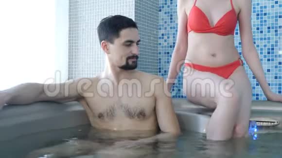 豪华酒店的健康水疗中心一对在按摩浴缸里放松穿着红色比基尼泳衣的漂亮苗条女人视频的预览图