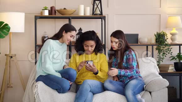 一群多种族女孩坐在家里看智能手机屏幕视频的预览图