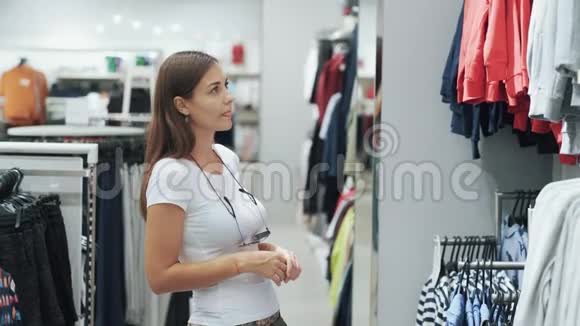 年轻女子在商场购物为孩子挑选衣服比较一下视频的预览图