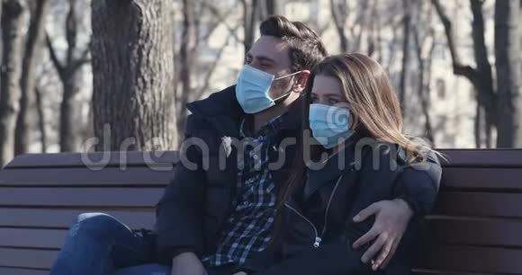 戴防护面具的年轻夫妇坐在公园的长凳上视频的预览图