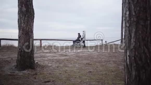 照相机接近坐在轮椅上的残疾青年和成年残疾人或与男子站在一起的母亲视频的预览图