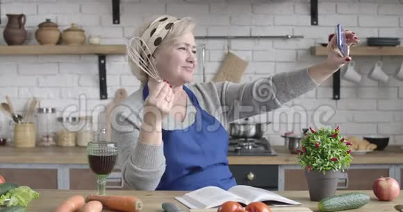 现代白种人女人在厨房里用烹饪工具做自拍开朗的女性退休者肖像视频的预览图