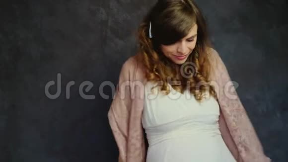 浪漫的白种人怀孕的年轻女子波浪般的头发微笑着站在黑暗的墙壁上跳舞视频的预览图