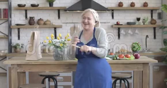 欢快的女性退休人员在室内用炊具跳舞和旋转的肖像微笑的白种人交叉双手视频的预览图