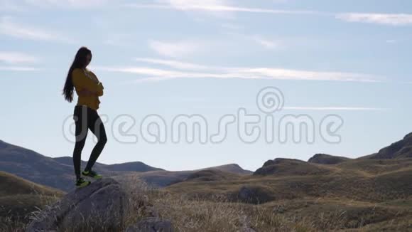 一个骄傲的美丽女孩在群山背景的石头上的剪影视频的预览图