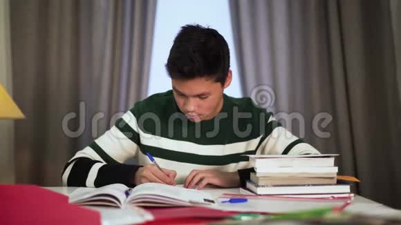 快乐的亚洲男孩在室内学习的肖像可爱的十几岁的大学生坐在桌子旁带着书和微笑视频的预览图