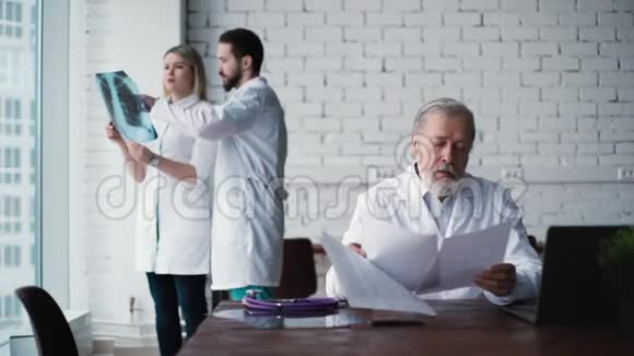 成人医生坐在他的办公桌上研究他的病人文件视频的预览图