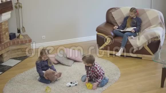 高瞻远瞩开朗的白种人兄妹在家玩作为他们的姐姐看书冷静的孩子视频的预览图