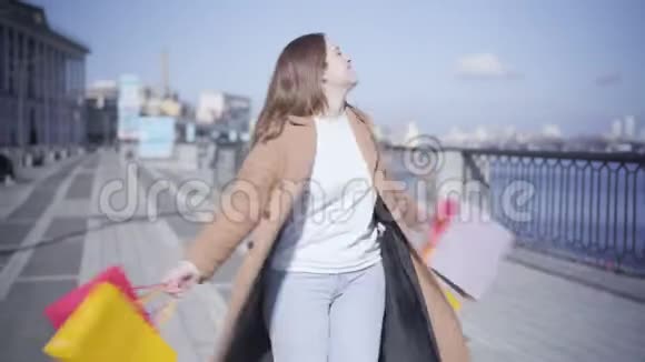 开朗胖乎乎的女人带着购物袋享受着阳光明媚的秋日快乐的白人女孩在旋转看着镜头视频的预览图
