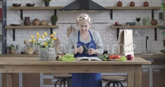 女性白种人退休后用菜刀剥黄瓜看食谱穿围裙做饭的老女人视频的预览图