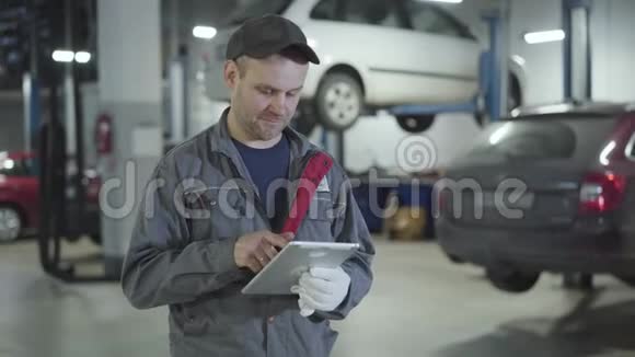自信的成年白种人男子使用平板电脑和显示拇指在相机在汽车修理店阳性男性汽车视频的预览图
