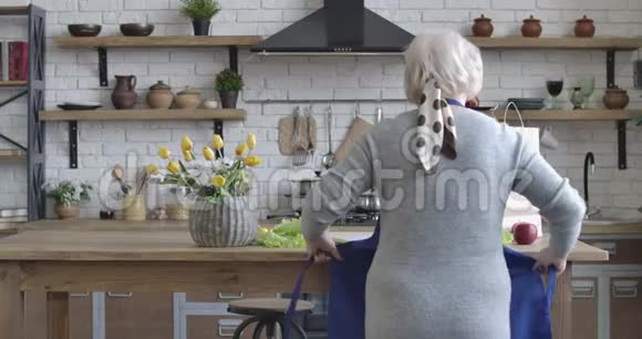 在现代厨房里穿着围裙的高加索女人的后景成年退休人员在视频的预览图
