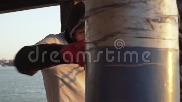 白人男孩拳击手在拳击梨上打户外拳击训练在河的背景上日落之光慢动作视频的预览图