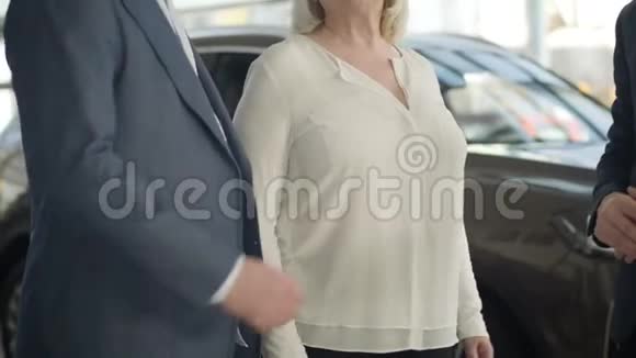 两个面目全非的白人男子西装革履地在成熟的金发女人面前握手站在汽车经销店视频的预览图