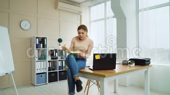 年轻的女商人坐在办公室桌上写着笔记本视频的预览图
