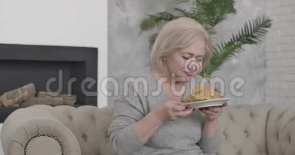 快乐的白人女性肖像棕色的眼睛闻着咬着美味的牛角面包积极的金发退休人员视频的预览图