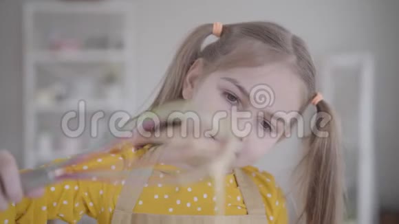 一张漂亮的白种人女孩特写的脸看着混合物滴出搅拌器可爱的小孩烤薄饼视频的预览图