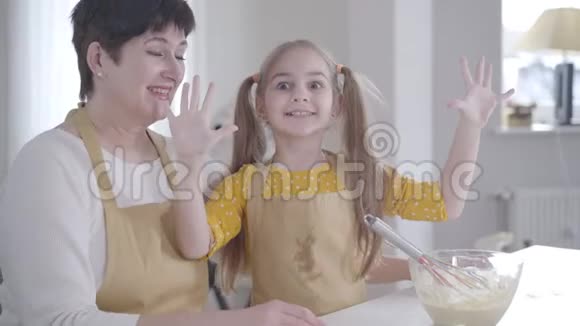 可爱的小女孩在厨房对着镜头做鬼脸奶奶在笑穿着围裙的白人孩子身上有脏东西视频的预览图
