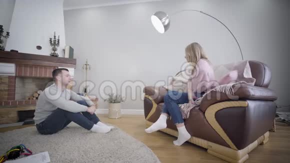 年轻的高加索家庭在室内享受周末男人坐在壁炉前的软地毯上妻子在玩视频的预览图