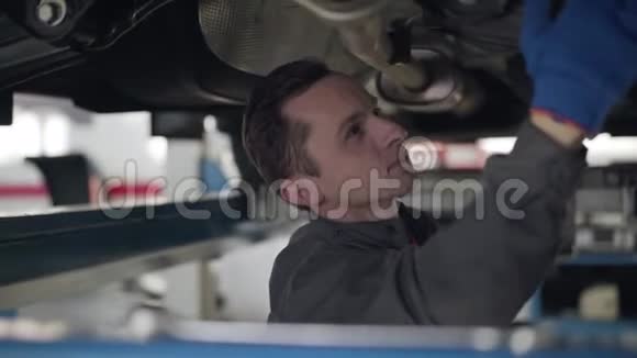 年轻白人检查车底的特写照片维修工程师在汽车修理厂工作视频的预览图