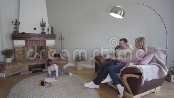 浅黑肤色的白种人小女孩坐在地板上画画她的父母坐在扶手椅上漂亮的女儿视频的预览图
