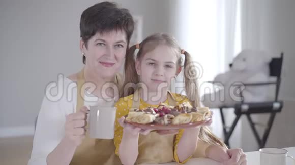 快乐的中年白种人女人对着镜头微笑拥抱着盘子里有煎饼的小漂亮女孩积极正面视频的预览图