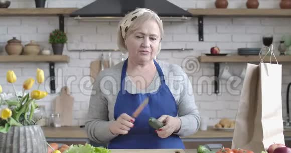 自信的高加索族女人在厨房里用黄瓜和刀子说话的肖像中年退休人员视频的预览图