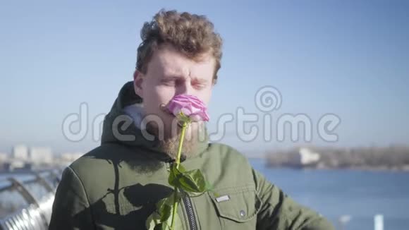一个年轻的白种人闻着粉红色的玫瑰看着手表带胡子的红发男友视频的预览图