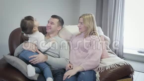 友好的高加索家庭坐在圈椅上在室内交谈微笑的金发女人年轻男人和小个子视频的预览图