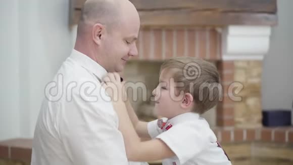 一个可爱的白人男孩帮父亲系蝴蝶结勤奋的孩子支持父母团结父亲视频的预览图