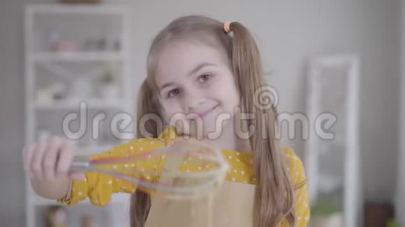漂亮的小白种人女孩棕色的眼睛在相机上微笑并从混合物中举起搅拌器进行烘焙漂亮的孩子视频的预览图