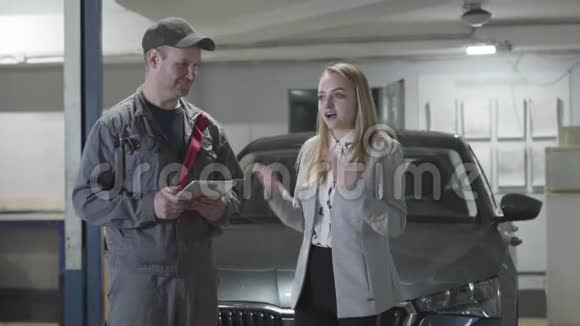 年轻的高加索女人在汽车修理店里有感情地交谈和手势令人兴奋的职业汽车小姐视频的预览图