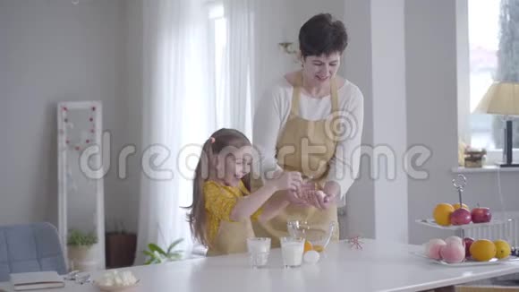 开朗的白人女孩帮助祖母在室内做饭小孙女笑着把鸡蛋打碎视频的预览图