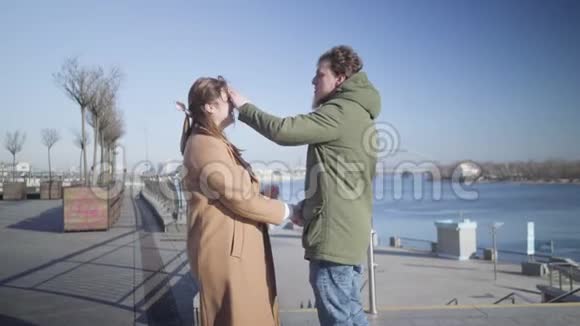 快乐微笑的白种人男人抚摸女朋友脸和固定她的头发的肖像年轻的情侣约会视频的预览图