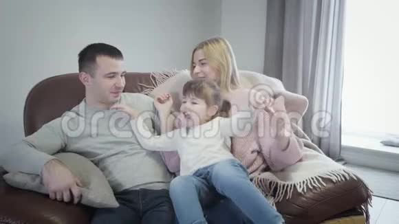 可爱的小白种人女孩坐在母亲手上然后拥抱父亲的肖像年轻的家庭享受快乐视频的预览图
