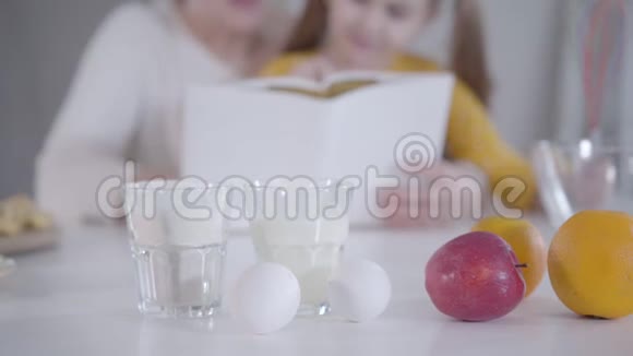 在桌子上特写牛奶鸡蛋面粉和水果背景下模糊的人在阅读食谱高加索人视频的预览图