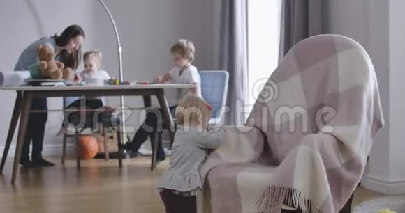 漂亮的金发女孩头上戴着红色的蝴蝶结从摇椅后面举起玩具她美丽的母亲妹妹和视频的预览图