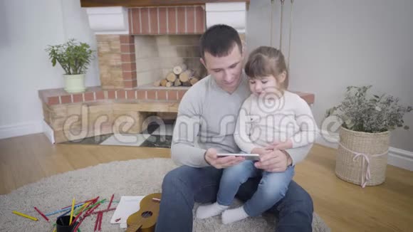 可爱的高加索小女孩和父亲坐在一起看智能手机上的卡通画年轻人享受平静视频的预览图