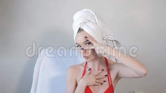穿着浴袍头上戴着白毛巾的年轻漂亮女人的肖像展示了她的手势和看镜头视频的预览图