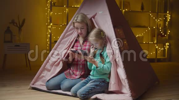 忙着打电话妈妈和孩子坐在小孩帐篷里视频的预览图