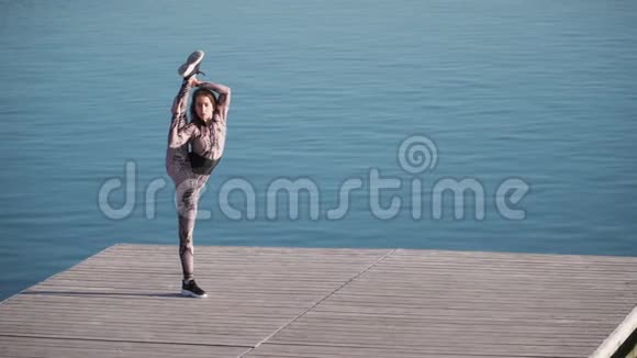 年轻的运动女孩有很大的伸展是码头上的分裂与蓝色的湖慢动作视频的预览图