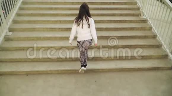 一个穿着白色夹克的年轻女孩跑上楼梯把他的手臂扔到一边慢动作视频的预览图